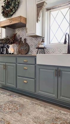 a kitchen with blue cabinets and white counter tops, an area rug and a wreath on the window sill