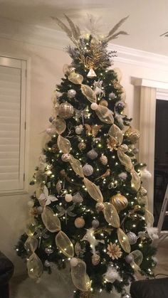 a decorated christmas tree in a living room with white and gold ornaments on the top