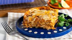 a piece of lasagna on a blue plate next to a salad and fork