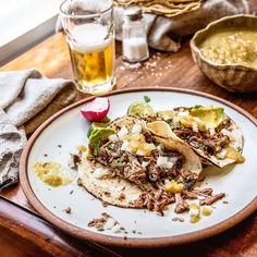 two tacos on a plate next to a glass of beer and some other food