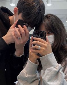 two people taking pictures with their cell phones in front of the camera while wearing masks