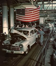 an old car being worked on in a factory with people looking at the cars hoods