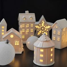 several small white houses are lit up with christmas lights on the windows and around them is a snowflake ornament