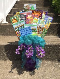 a purple vase filled with lots of books on top of some steps next to flowers