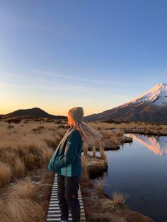 a woman is standing on a path near a body of water with a mountain in the background