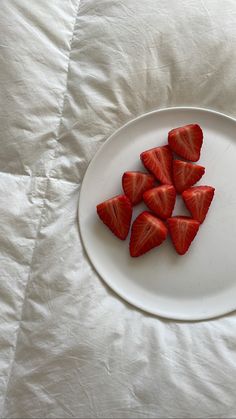 strawberries are arranged on a white plate on a bed with white sheets in the background