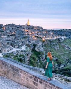 a woman standing on the edge of a stone wall looking at an old town in the distance