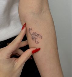 a woman's arm with a small scorpion tattoo on the left side of her arm