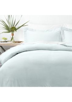 a bed with blue sheets and pillows on top of it next to a potted plant