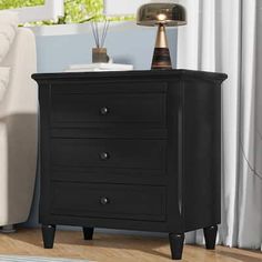 a black night stand with two drawers and a lamp on it in front of a white couch