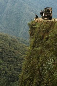 two jeeps are parked on the edge of a cliff with mountains in the background