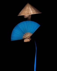 a woman holding a blue fan in her hand with a hat on top of her head