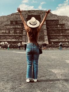 a woman standing in front of an ancient structure with her arms raised up to the sky