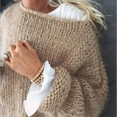 a woman with blonde hair wearing a sweater and bracelets