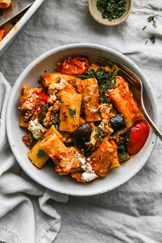 a bowl filled with pasta and vegetables on top of a white cloth next to a fork