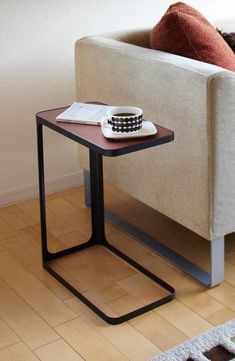 a small table with a bowl on it in front of a white couch and wooden floor