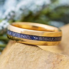 two yellow gold wedding bands with blue lapis inlays on top of a rock