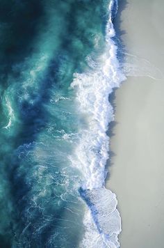 an aerial view of the ocean with waves coming in to shore and people walking on the beach