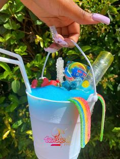 a person holding a bucket filled with blue liquid and candy on top of green bushes