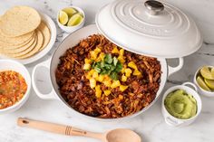 a large pot filled with food next to bowls of salsa and tortillas