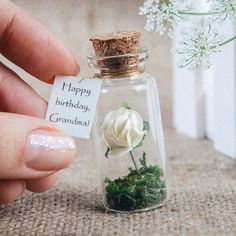 someone is holding a tiny glass bottle with flowers in it that says happy birthday grandma