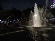 people are gathered around the water fountain at night