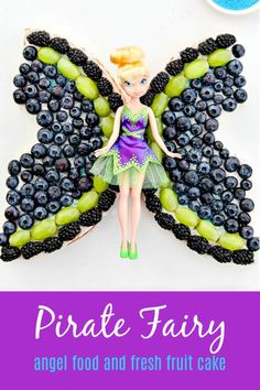 a fairy cake is decorated with grapes, blueberries and a butterfly shaped tinker