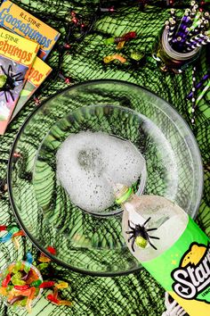 a glass bowl filled with liquid next to halloween decorations and books on a green table cloth