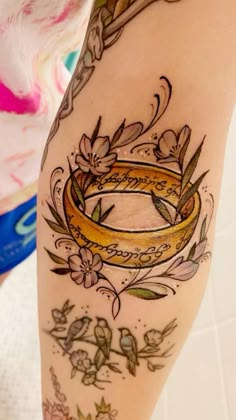 a woman's leg with tattoos on it and a gold ring in the middle