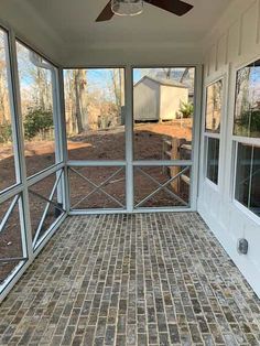 an enclosed porch with brick flooring and ceiling fan on the side of the room