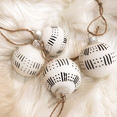 three white ornaments with black designs on them sitting on a fur covered surface and tied in twine