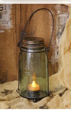 a glass lantern with a lit candle in it sitting on a cloth covered tablecloth