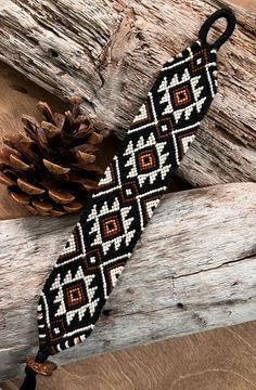 a black and white beaded tie next to a pine cone on wooden planks