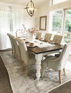 a dining room table with chairs and a rug in front of the window that is open