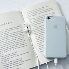 an open book with headphones and earbuds on it next to an iphone