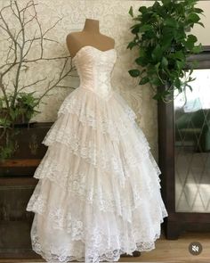 a white wedding dress is on display in front of a mirror and potted plant