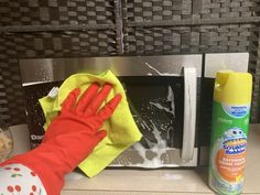 a person cleaning a microwave with a yellow rag and orange mitt on the counter