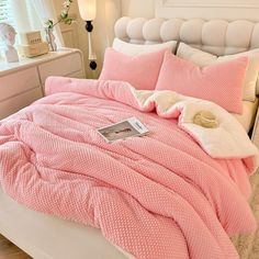 a bed with pink comforter and pillows on it in a bedroom next to a white headboard