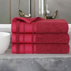 three red towels stacked on top of each other in front of a sink and mirror