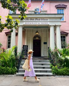 a woman walking in front of the old pink house restaurant and tavern, with flags flying overhead