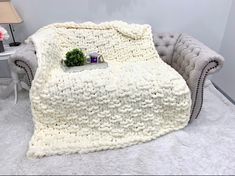 a white blanket sitting on top of a couch next to a table with a potted plant