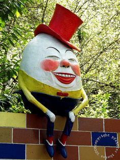 a statue of a smiling man sitting on top of a brick wall