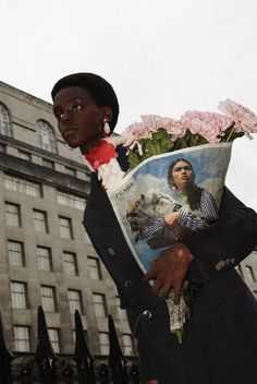 a woman holding flowers in front of a building with a large poster on it's back