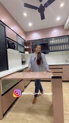 a woman is standing in the middle of a kitchen with an island and ceiling fan