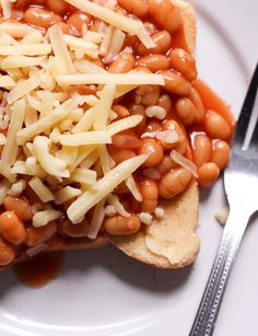 a white plate topped with beans and cheese next to a fork on top of a table