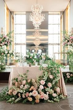 a table with flowers and greenery on it in front of a chandelier