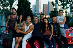 a group of people sitting on top of a red car in front of a city