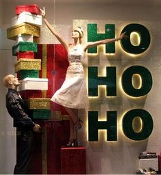 a man standing next to a woman in front of a shop window with presents on display