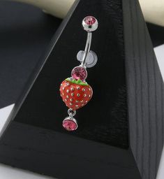 a red strawberry belly button ring with pink and white polka dots on the bottom, attached to a black wooden stand