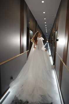 a woman in a white wedding dress is walking down the hallway